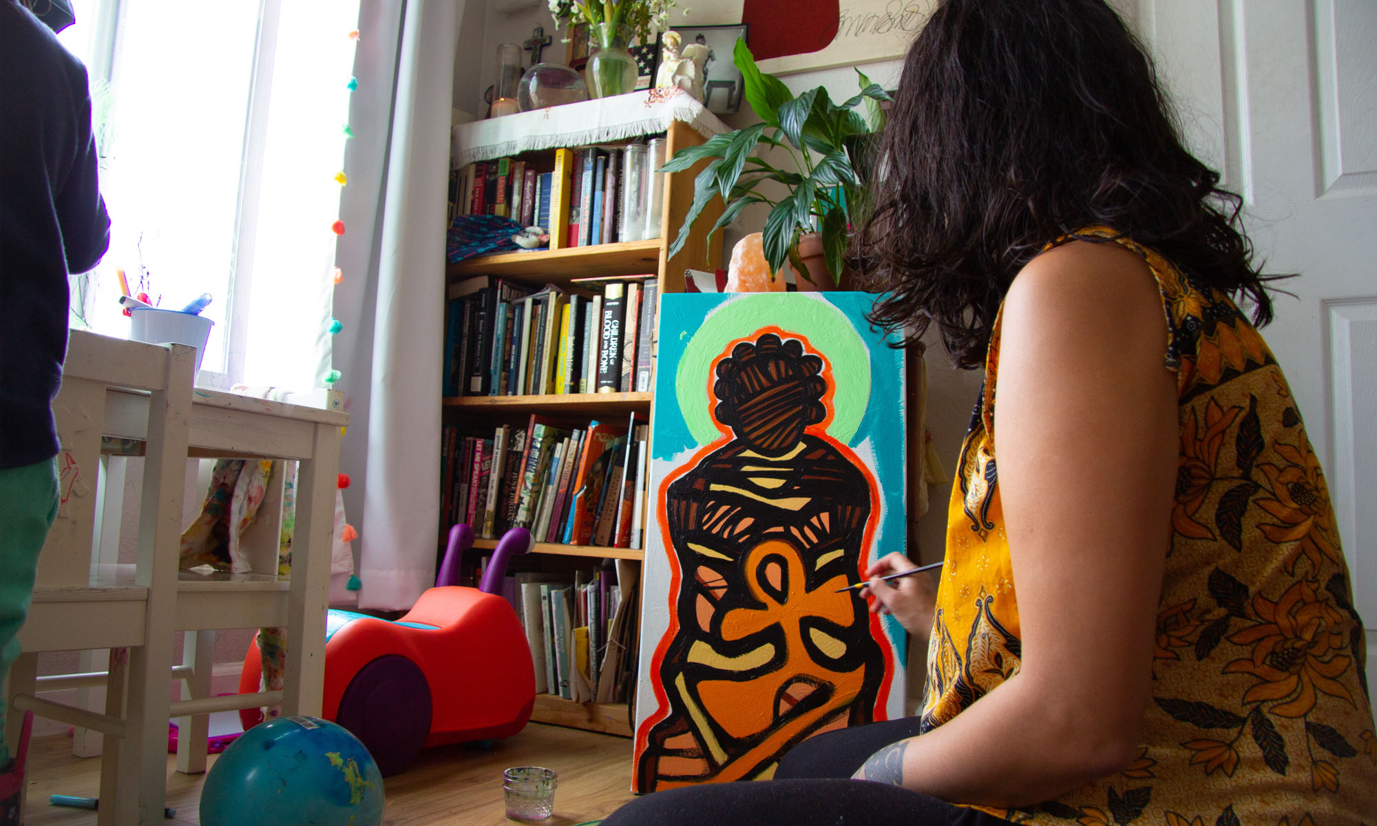 Artist Francis sits on the floor of her living room and adds the final touches to a painting of a Black person holding an Ankh. Photo: Kathryn Styer