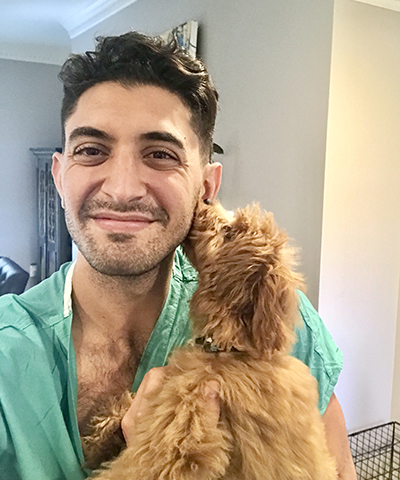 Dr. Khatib pictured from the chest up smiling, wearing light green scrubs and holding a brown puppy.